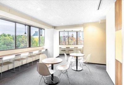 Communal breakout area with round cafe tables and large windows overlooking city greenery.