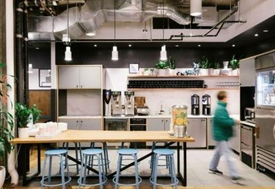 Sleek office kitchen and pantry area with a long wooden breakfast bar and blue stools.