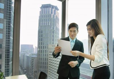 Two business professionals reviewing paperwork in front of a floor-to-ceiling city view window.