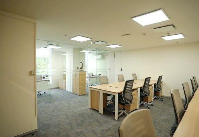 Open-plan office space with wooden desks and ergonomic black chairs.
