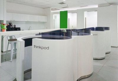 Communal breakout area with white curved privacy pods and a kitchen in the background.