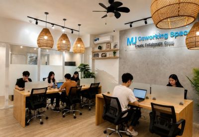Bright coworking lounge with people working at long wooden tables under woven pendant lights.