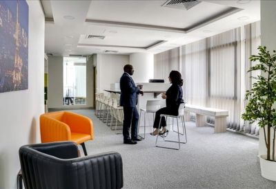 Bright coworking area with orange and black lounge chairs and people chatting at a high table.