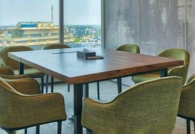 Glass-walled meeting room with a wooden table and green upholstered chairs overlooking city views.