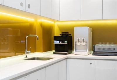 Modern office kitchen with white cabinetry, coffee machine, and yellow splashback.
