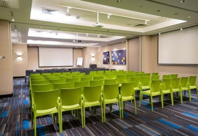 Large professional seminar room with rows of green chairs and projector screens.