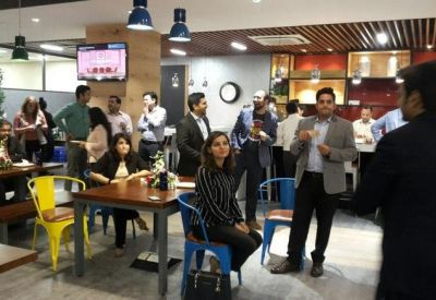 Lively communal breakout space with people gathering near wooden tables and colorful chairs.