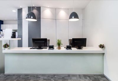 Bright reception desk with minimalist white finishes, dual monitors, and pendant lights.