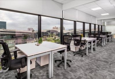 Open-plan office with white desks and floor-to-ceiling windows showing city views.
