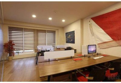 Bright workspace featuring wooden desks, ergonomic chairs, and a large red wall banner.