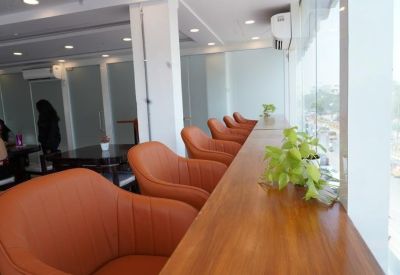 Lounge area with tan leather armchairs arranged along a wooden window counter with plants.