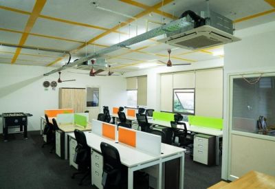 Spacious office layout with rows of desks, colorful dividers, and ceiling-mounted AC units.
