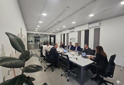 Professional meeting room with people seated around a large white conference table.
