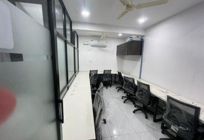 Bright workspace featuring rows of white desks and black ergonomic chairs against a frosted glass partition.