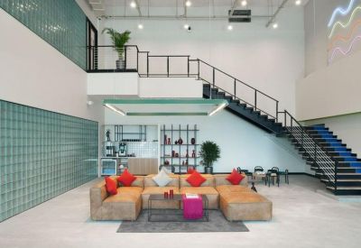 Spacious communal lounge with a tan sectional sofa, industrial staircase, and glass-block wall.