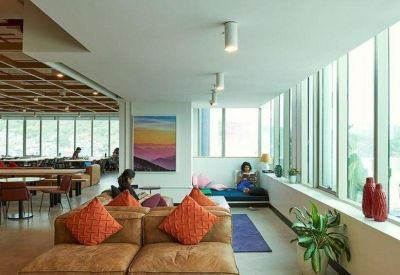 Sunlit coworking space featuring tan leather seating, orange pillows, and a scenic wall painting.