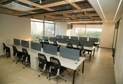 Modern open-plan office with white desks, ergonomic chairs, and large windows.