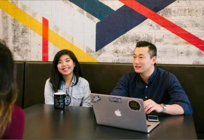 Casual meeting area featuring a geometric mural and people collaborating at a table with a laptop.