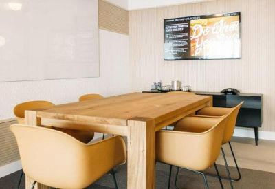 Modern meeting room with a wooden table, tan chairs, and a whiteboard.