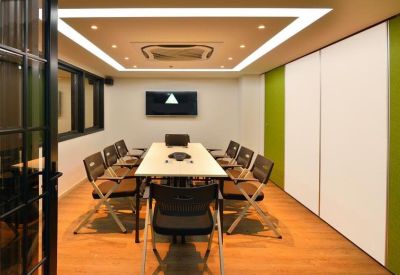 Well-lit meeting room with a long table and black chairs featuring a green accent wall.