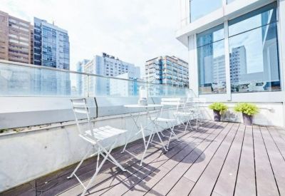 Outdoor roof terrace with white folding chairs, wooden decking, and views of the surrounding city skyline.