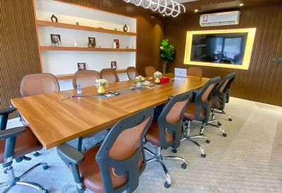 Large boardroom with a wood-finished table, ergonomic chairs, and wall shelving.