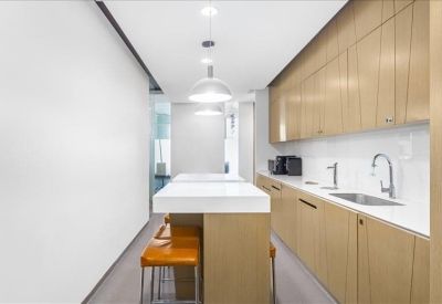 Modern communal kitchen area with light wood cabinets and a white breakfast bar.