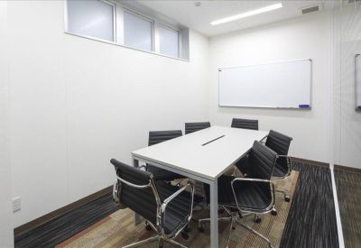 Professional meeting room featuring a white boardroom table and six black leather chairs.