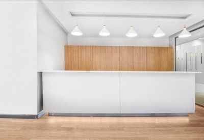 Minimalist reception area with a long white desk, wood-paneled wall, and pendant lighting.