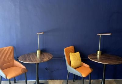 Two cafe-style round wooden tables with orange and grey chairs against a deep blue feature wall.