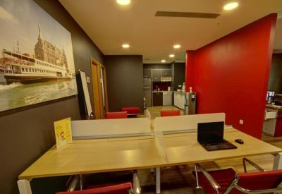Common area with workstations, a red feature wall, and a kitchen area in the background.