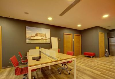 Open-plan coworking area with light wood desks, red chairs, and a large mural.