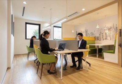 Open-plan coworking space with partitioned desks and green accent chairs.