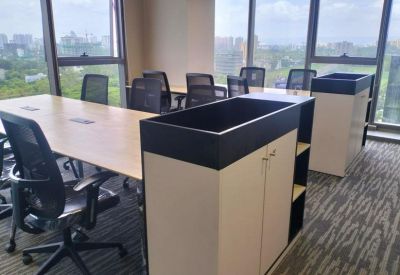 Open-plan office space with light wood desks, mesh chairs, and large windows overlooking the city.