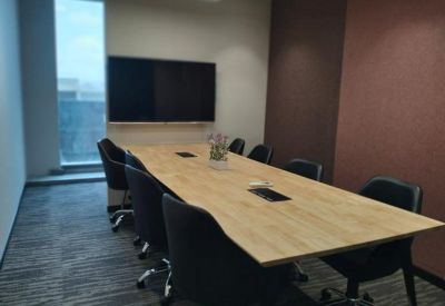 Modern meeting room with a light wood table, black ergonomic chairs, and a large wall-mounted screen.