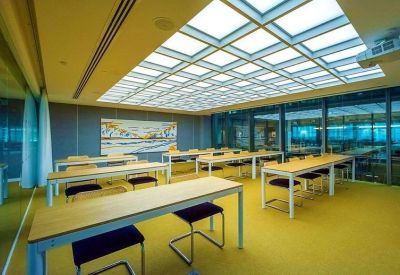Flexible training room with rows of light wood desks and yellow flooring under a skylight.