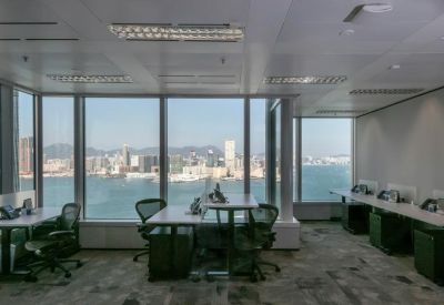 Open-plan office workspace featuring desks with a panoramic harbor view through floor-to-ceiling windows.