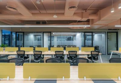 Bright open-plan workspace with long wooden desks and yellow privacy dividers.