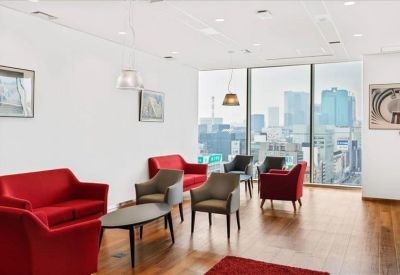 Modern breakout area featuring red sofas, grey armchairs, and expansive city skyline views.