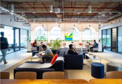 Modern communal coworking space with diverse seating, low tables, and exposed ceiling pipes.
