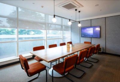 Bright boardroom with a wooden table, orange chairs, and a large wall-mounted monitor.