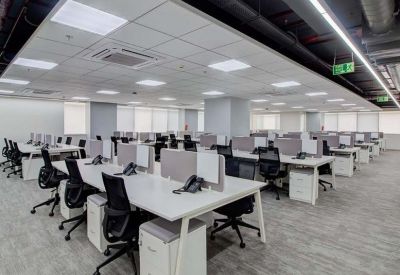 Spacious open-plan office with rows of white desks and ergonomic black chairs.