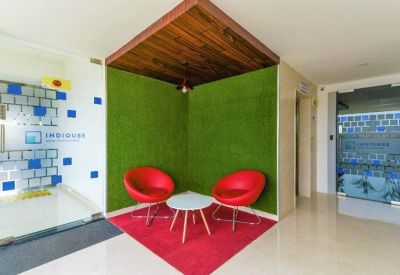 Modern reception waiting area with red chairs, a green turf wall, and wood ceiling accents.