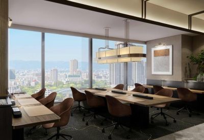 Long wooden coworking table with ergonomic chairs and city skyline views through large windows.