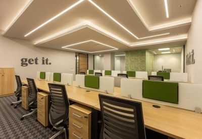 Open-plan workspace with wooden desks, green privacy screens, and tiered ceiling lighting.