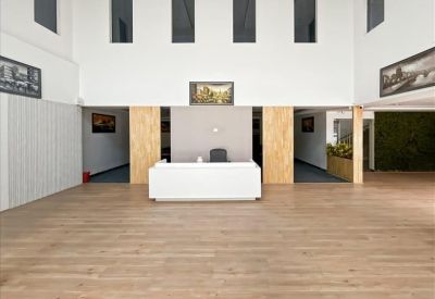 Wide reception lobby with light wood flooring and a minimalist white front desk.