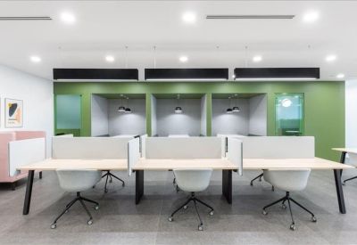 Open-plan workspace with long white desks and private green acoustic booths in the background.