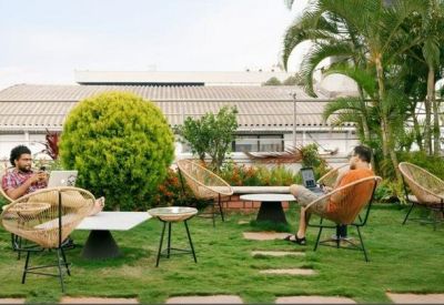 Lush rooftop terrace garden with wicker chairs and small tables on a green lawn.