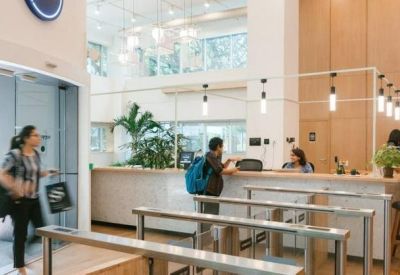 Bright, high-ceilinged reception area with wooden paneling, indoor plants, and security turnstiles.