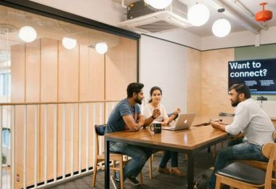 Modern meeting space with people working at a wooden table under warm pendant lighting.